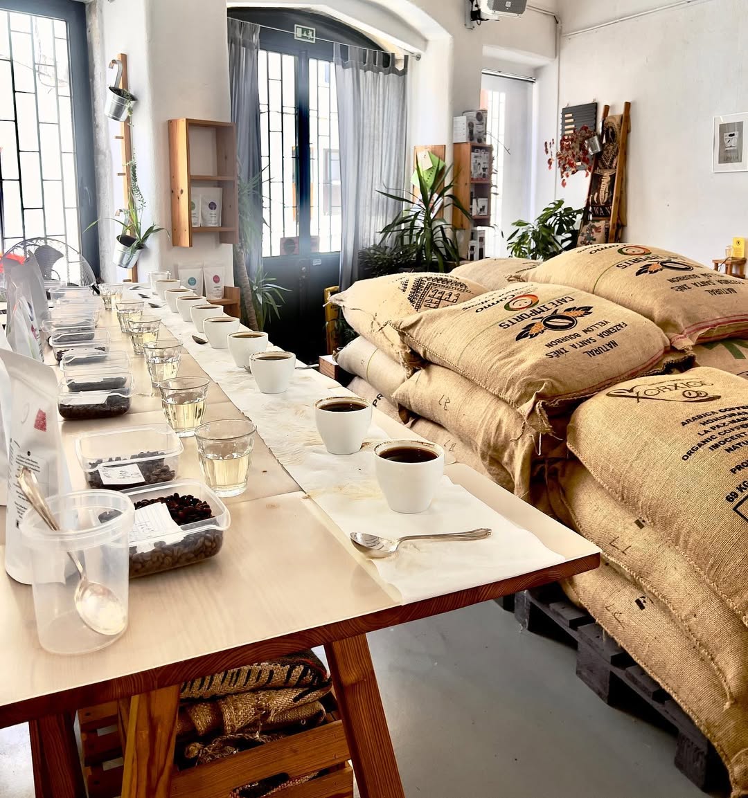 Mesa comprida de madeira com sacos de café ao fundo